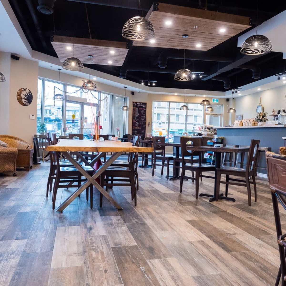 A modern café interior with wooden tables, chairs, and large windows allowing natural light to illuminate the space.