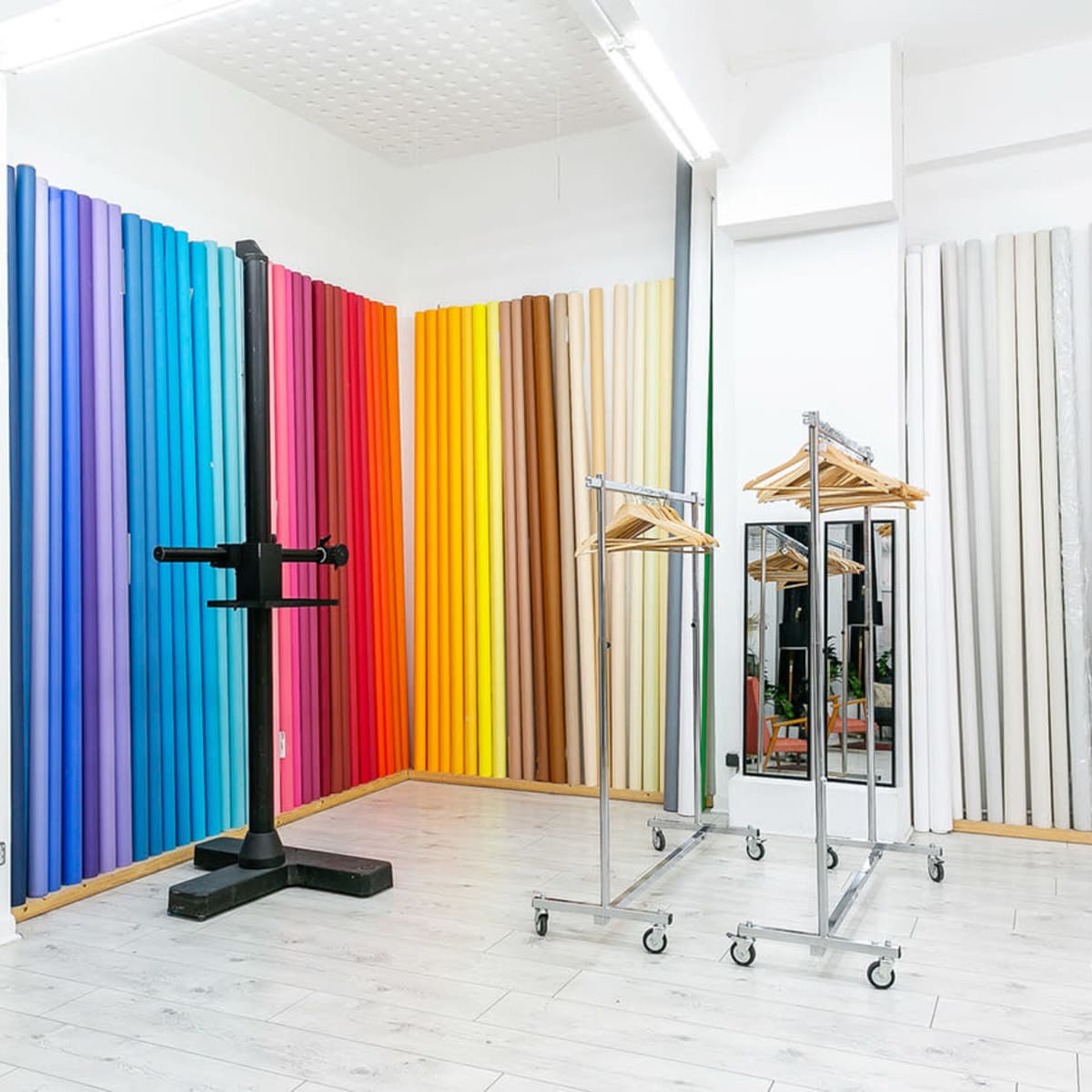 A studio with colorful roll-backdrops on the walls, a clothing rack on wheels, and a stand for photography.