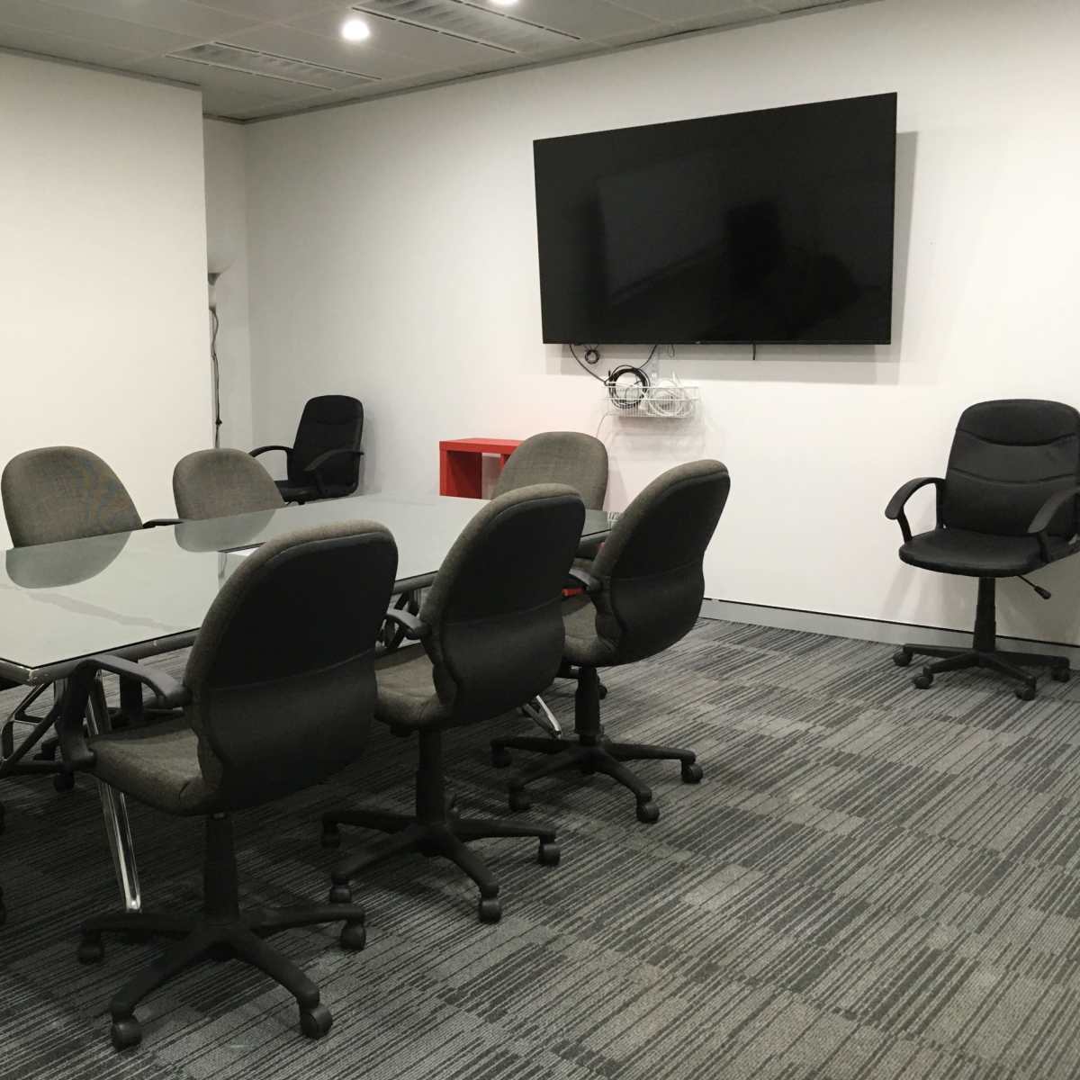 A conference room with a glass-topped table surrounded by eight upholstered chairs, a whiteboard, and a wall-mounted television.