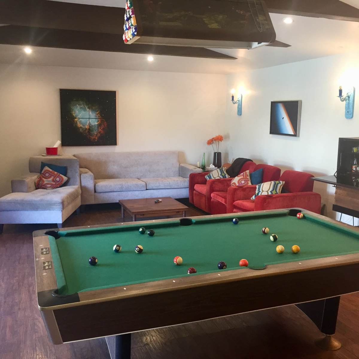 A game room featuring a pool table, a sofa, two red chairs, and a bar cabinet against the wall.