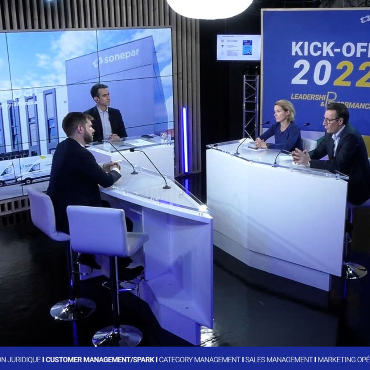 A panel of four people discusses business strategies in a modern studio setting, with a large graphic displaying "KICK-OFF 2022" in the background.