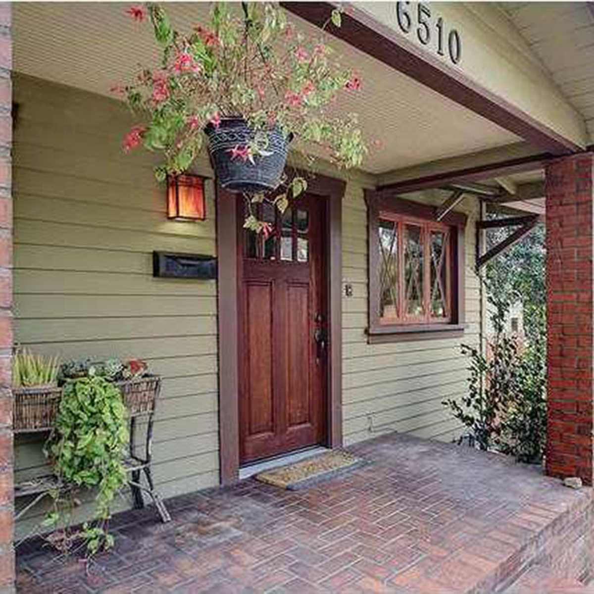 The entrance of a house with a wooden front door, brick accents, and potted plants on the porch.
