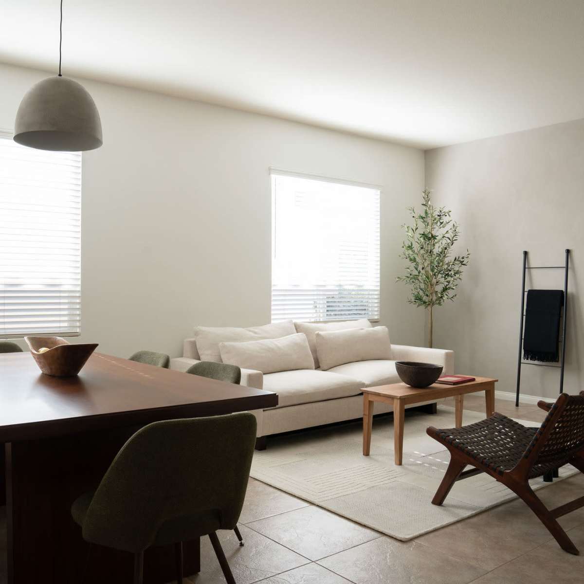 A modern living space features a light-colored sofa, a wooden dining table, and several chairs arranged around a neutral rug.