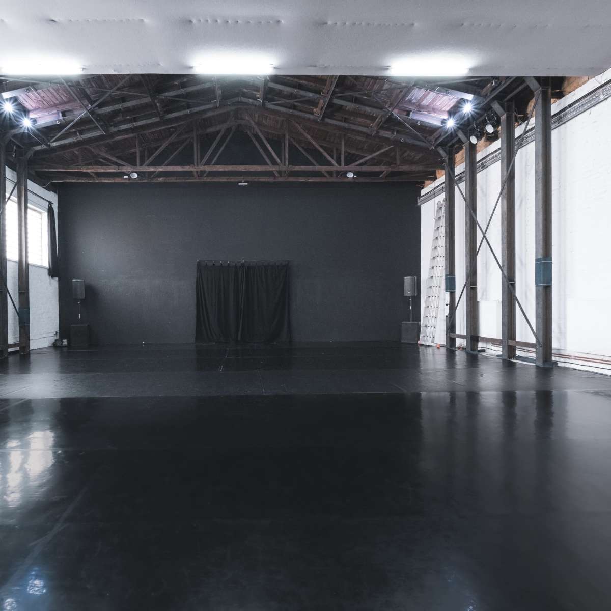 A large, empty studio space with polished black flooring and high wooden beams.