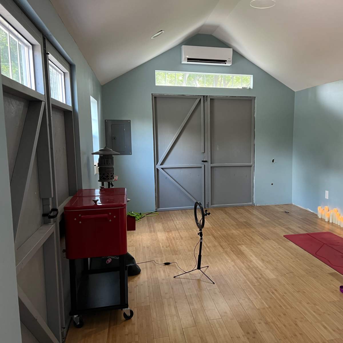 A serene room with bamboo flooring, featuring a yoga mat, a small cart, and a row of candles along the wall.