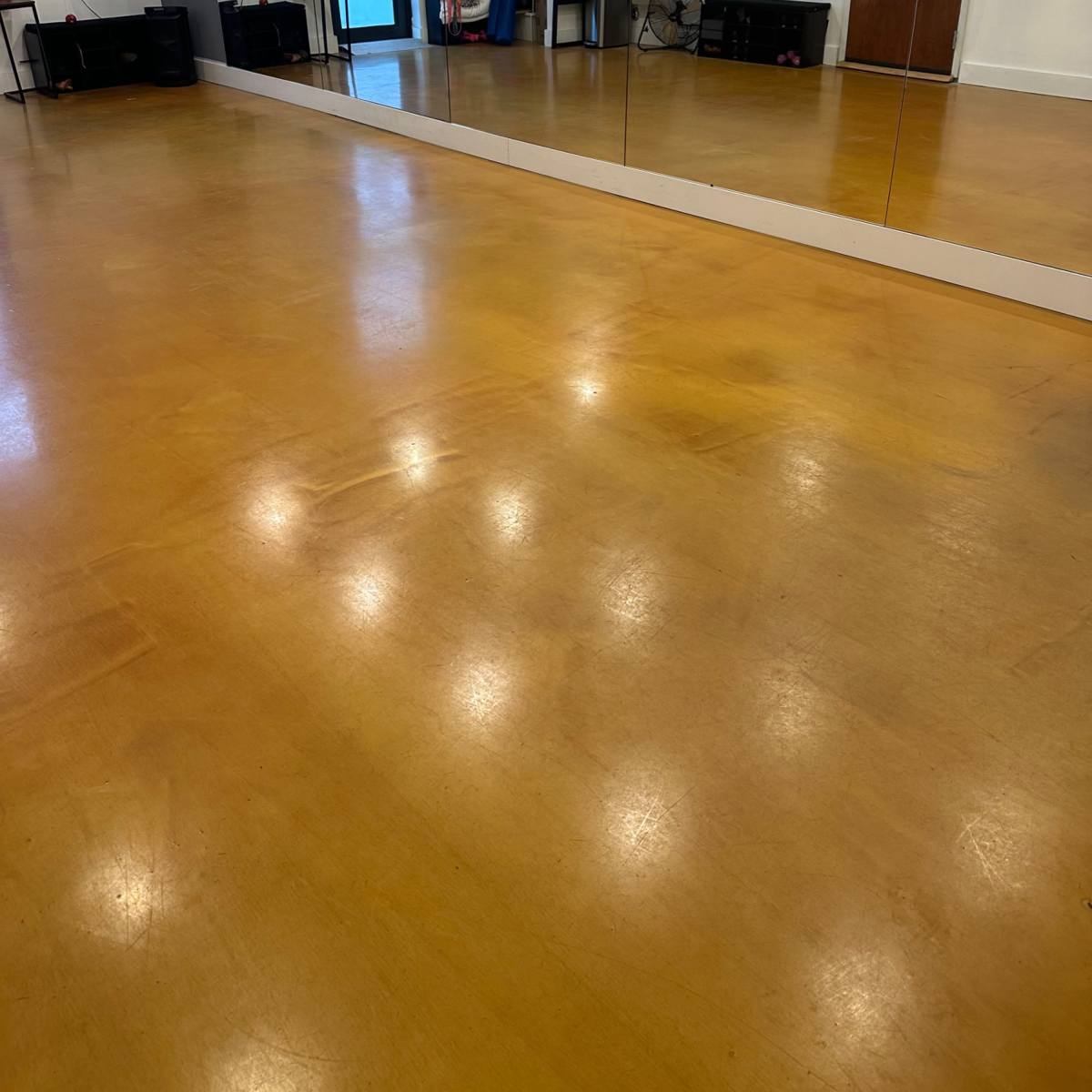 An empty room with polished yellow floors, a large mirror on one wall, and a door leading outside.