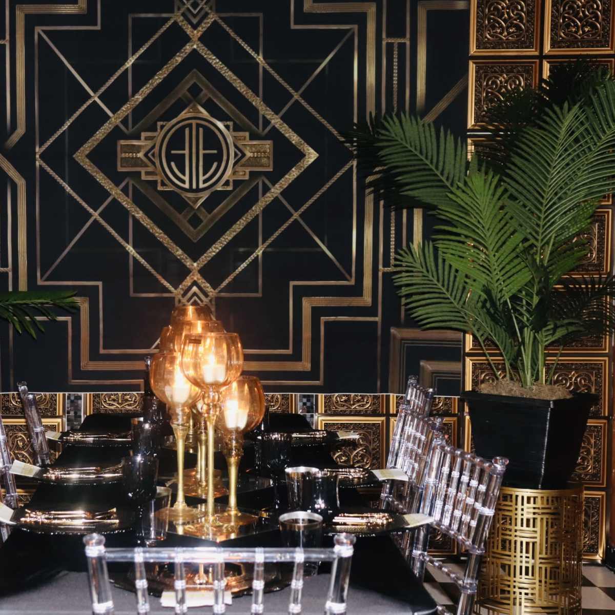 An elegantly designed dining room featuring a black and gold geometric wall pattern, a glass dining table, and decorative plants in planters.