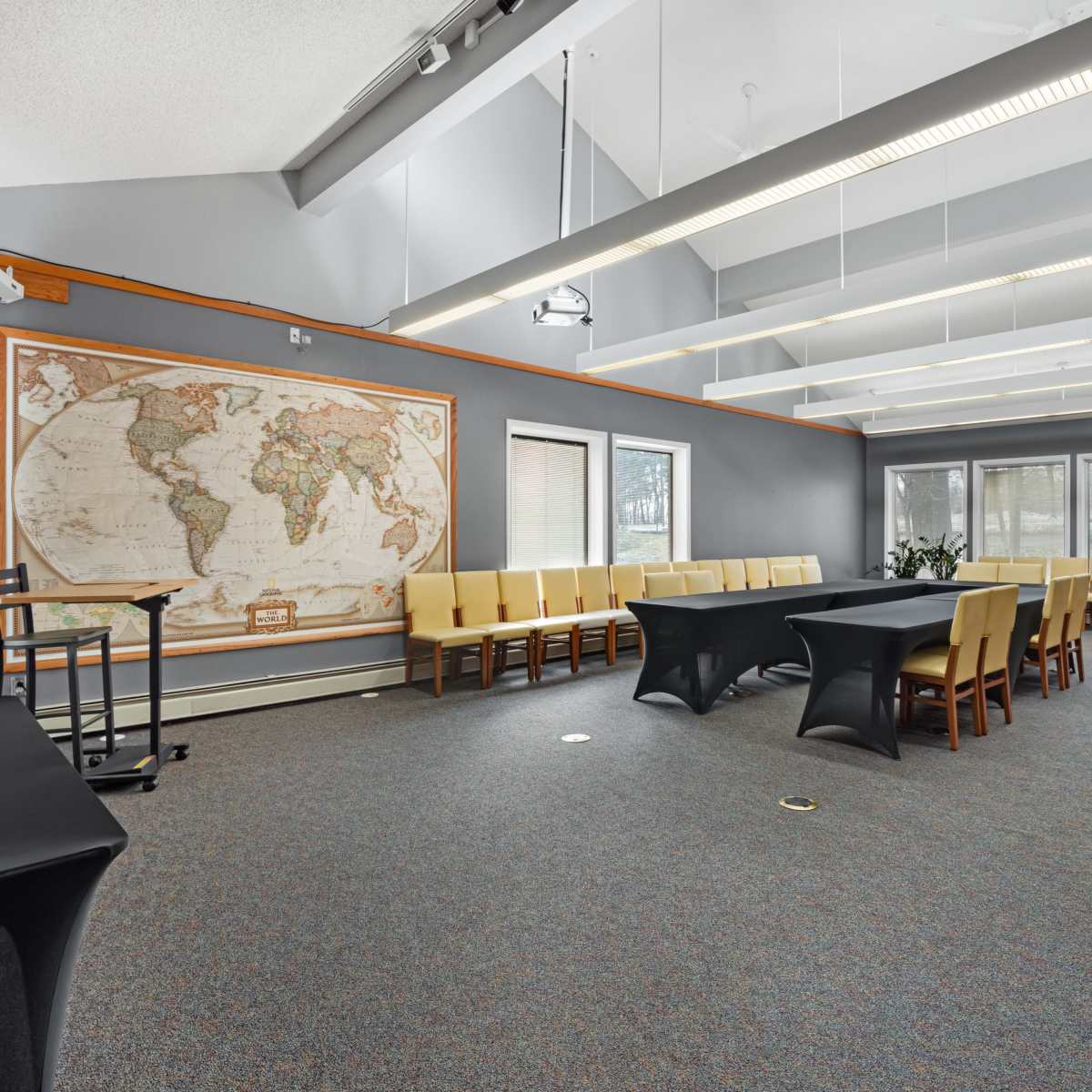 A well-lit conference room featuring a large world map on the wall, a central black table surrounded by chairs, and windows allowing natural light.