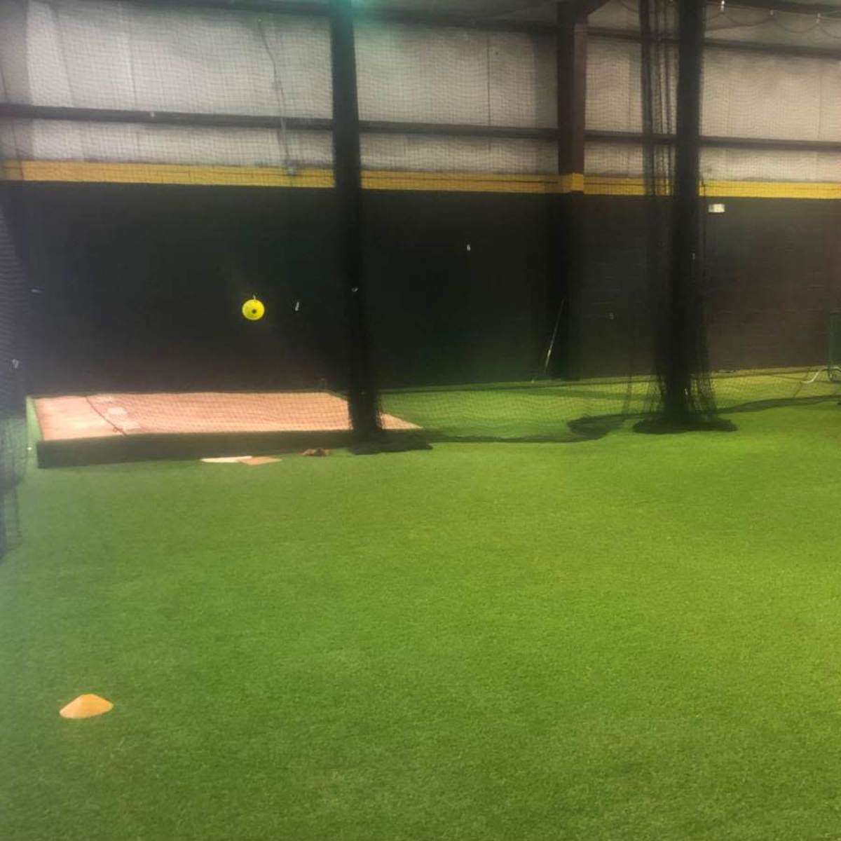 An indoor sports facility with artificial turf, batting cages on the left, and a pitching area in the back.