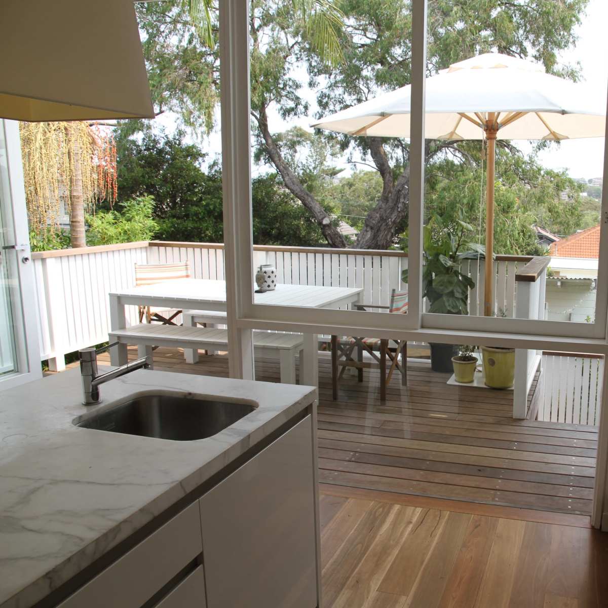 A modern kitchen with a view of a wooden deck and patio umbrella through large glass doors.