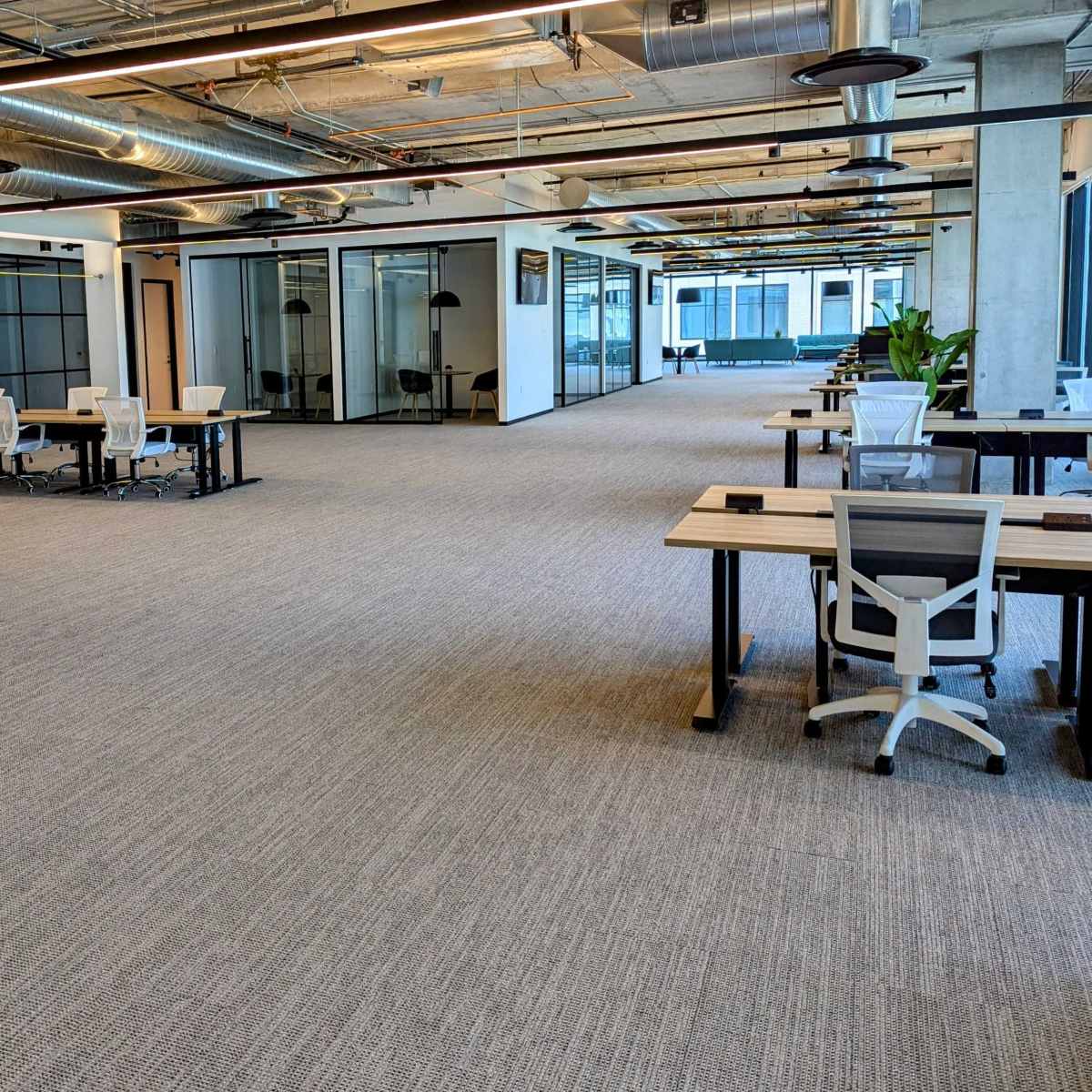 An open office space features rows of desks and chairs with glass-walled meeting rooms in the background.