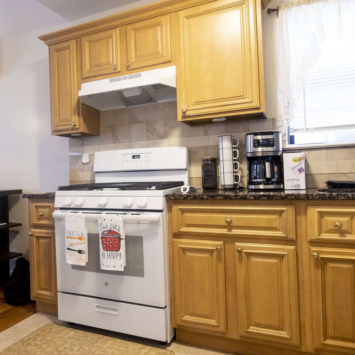 A kitchen with wooden cabinets, a gas stove, a microwave above it, and various appliances on the countertop, including a coffee maker.