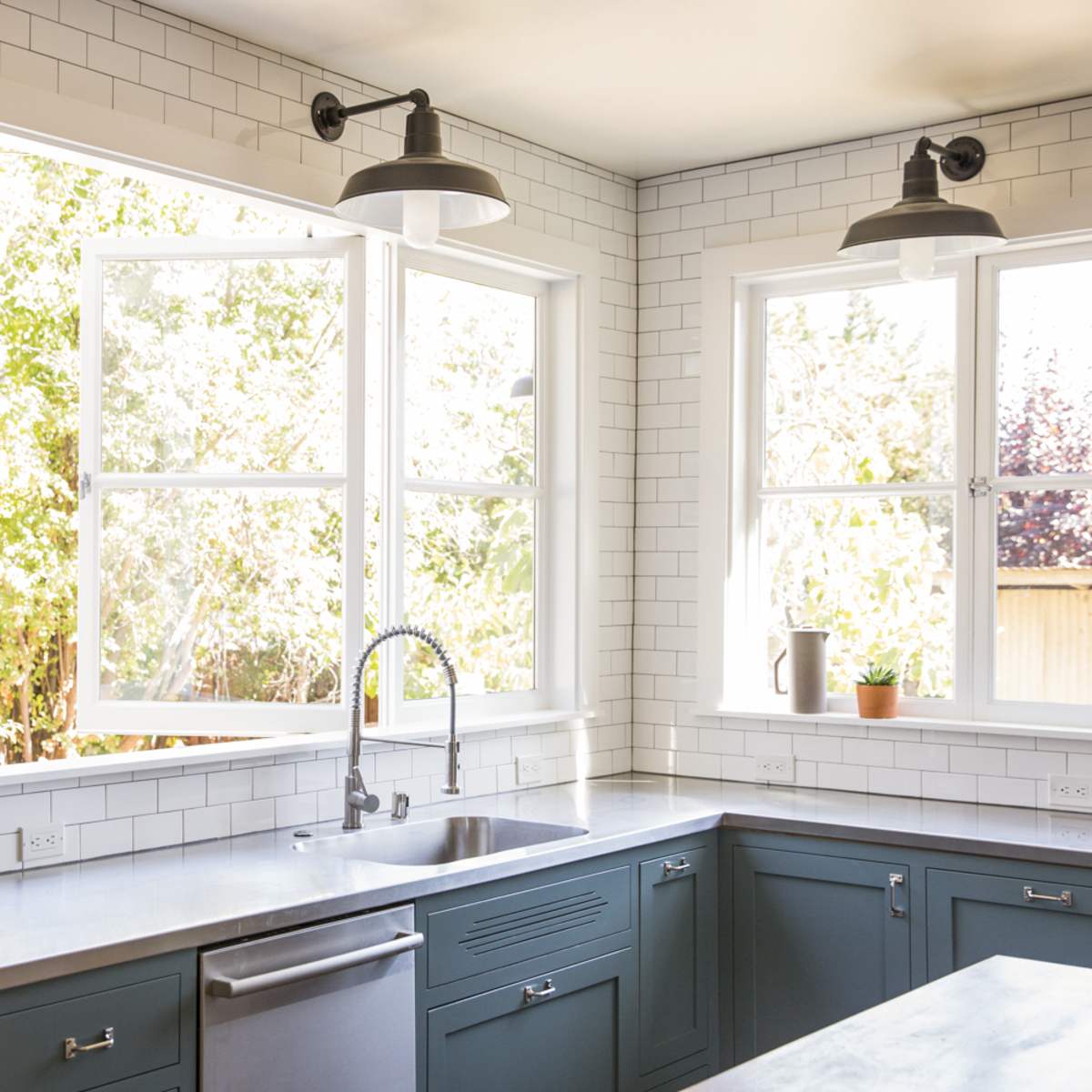 A modern kitchen features teal cabinets, a stainless steel sink, and large windows allowing natural light to enter.