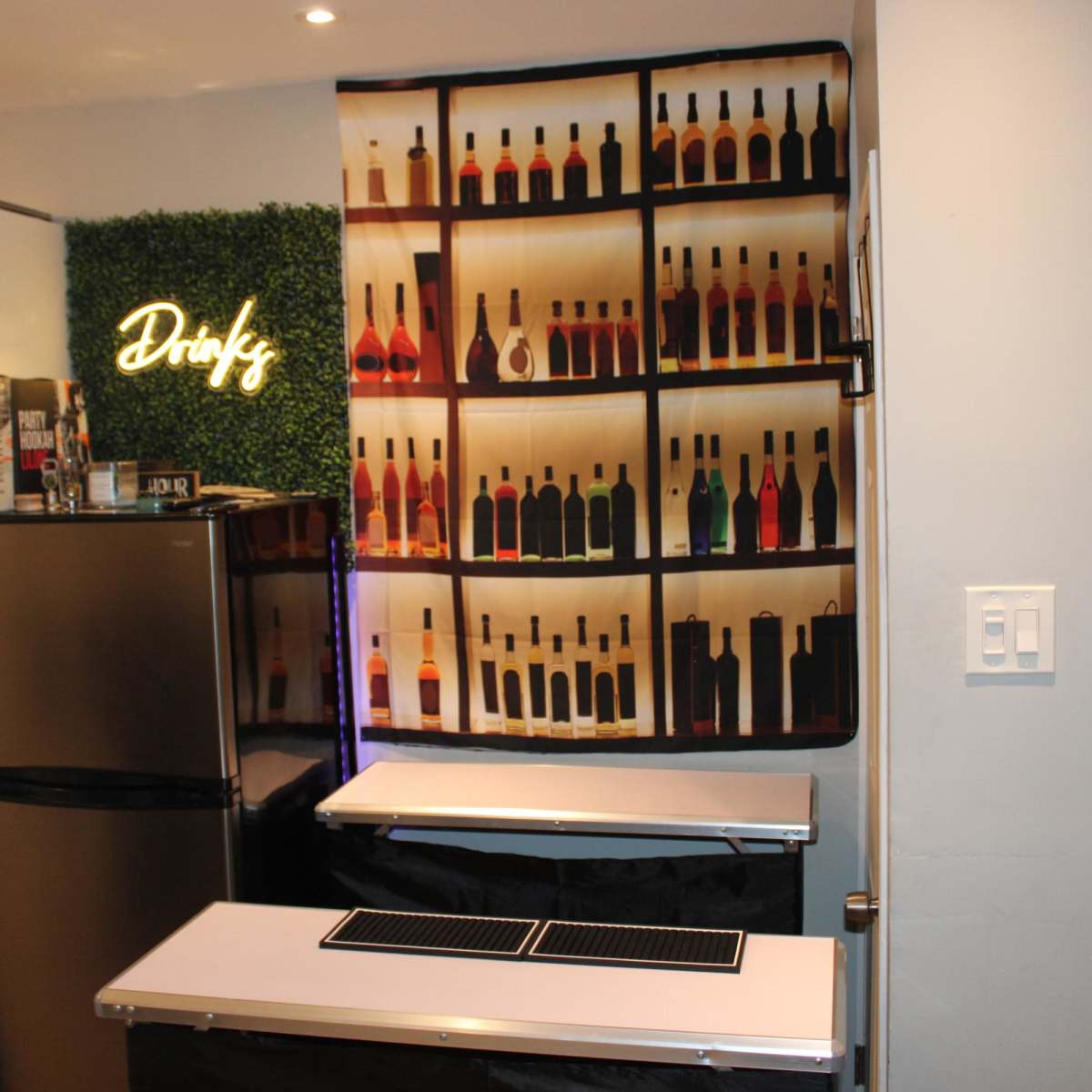 A kitchen area featuring a curtain with a design of various bottles on a shelf, next to a refrigerator and a bar top with two serving areas.