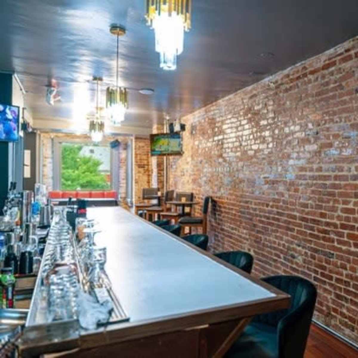 A bar area with a long countertop and exposed brick walls, leading to a window with a view of greenery outside.