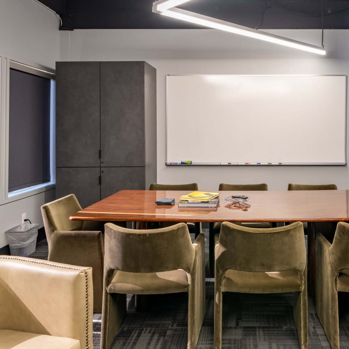 A modern conference room features a large wooden table surrounded by eight green chairs and a whiteboard on the wall.