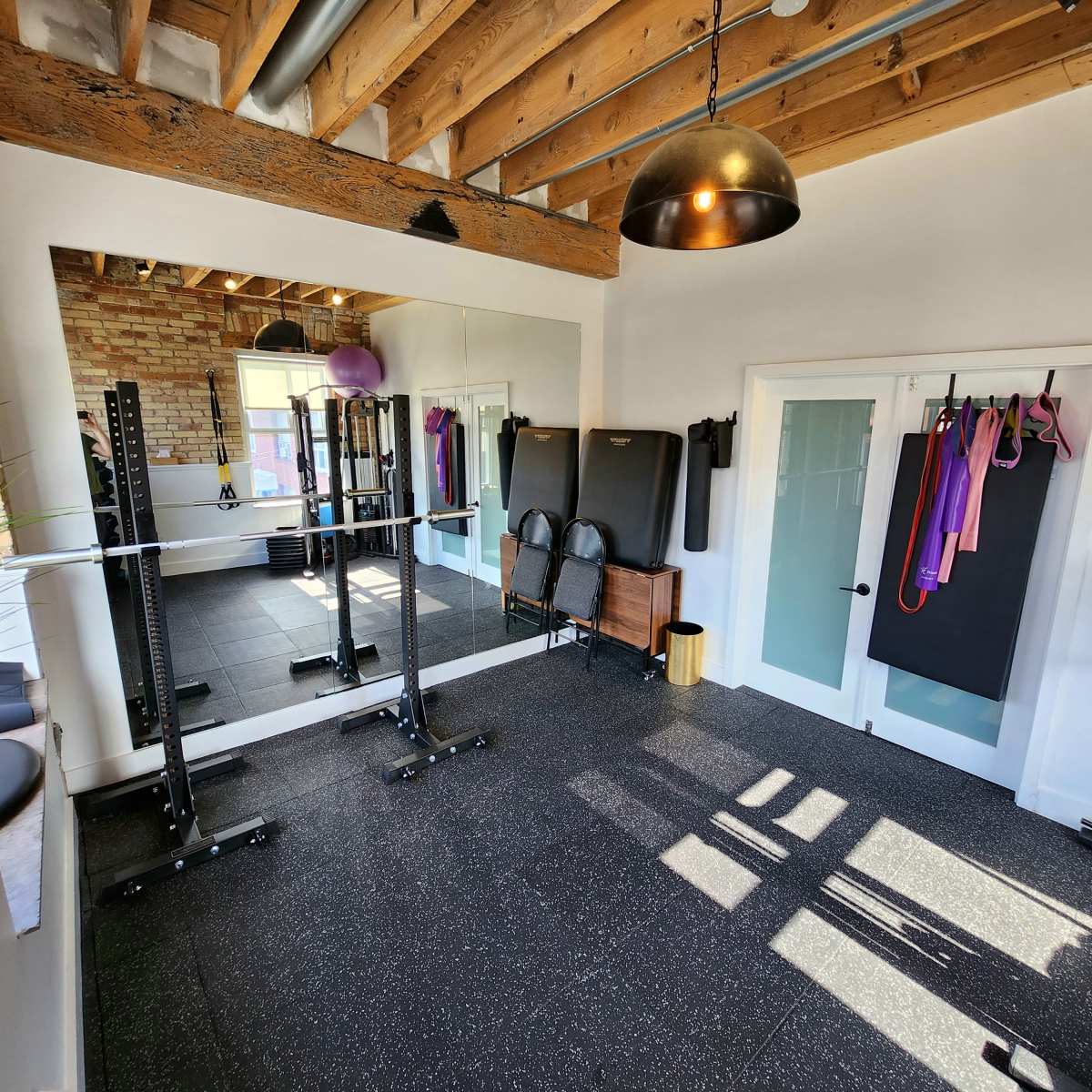 A well-lit home gym with a mirrored wall, exercise equipment, and a wooden beam ceiling.