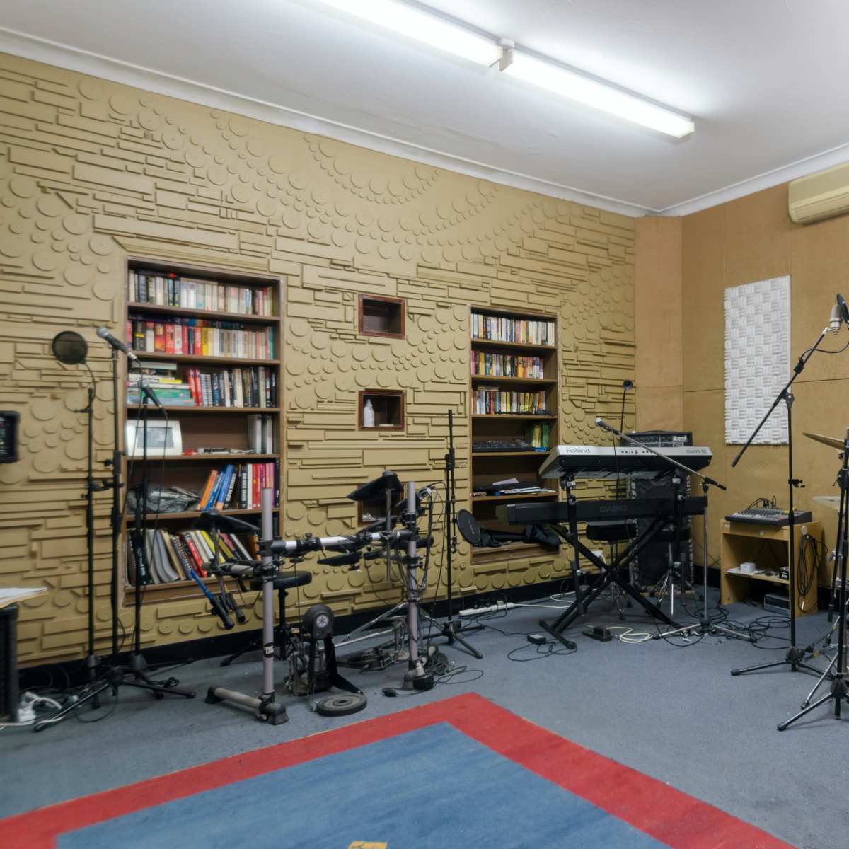 A music recording studio with a variety of instruments, including a drum set, keyboard, and electronic drum pads, alongside soundproofing panels on the walls.