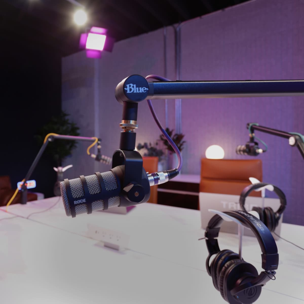 A modern podcasting studio features a Blue microphone mounted on an adjustable arm, with headphones and a laptop on a sleek table, illuminated by soft lights.