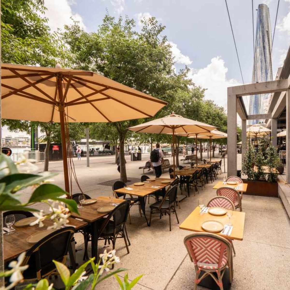 An outdoor dining area with tables, chairs, and umbrellas lined along a sidewalk beside a restaurant.