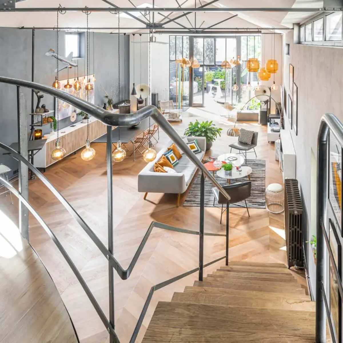 A modern interior space featuring an open layout with a staircase, large windows, and stylish furniture arrangements.