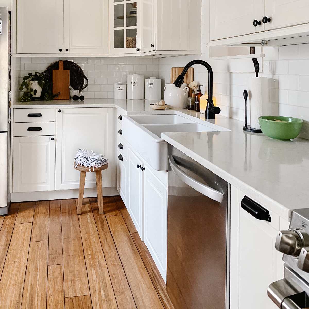 A bright kitchen features white cabinetry, a farmhouse sink, and wooden flooring.