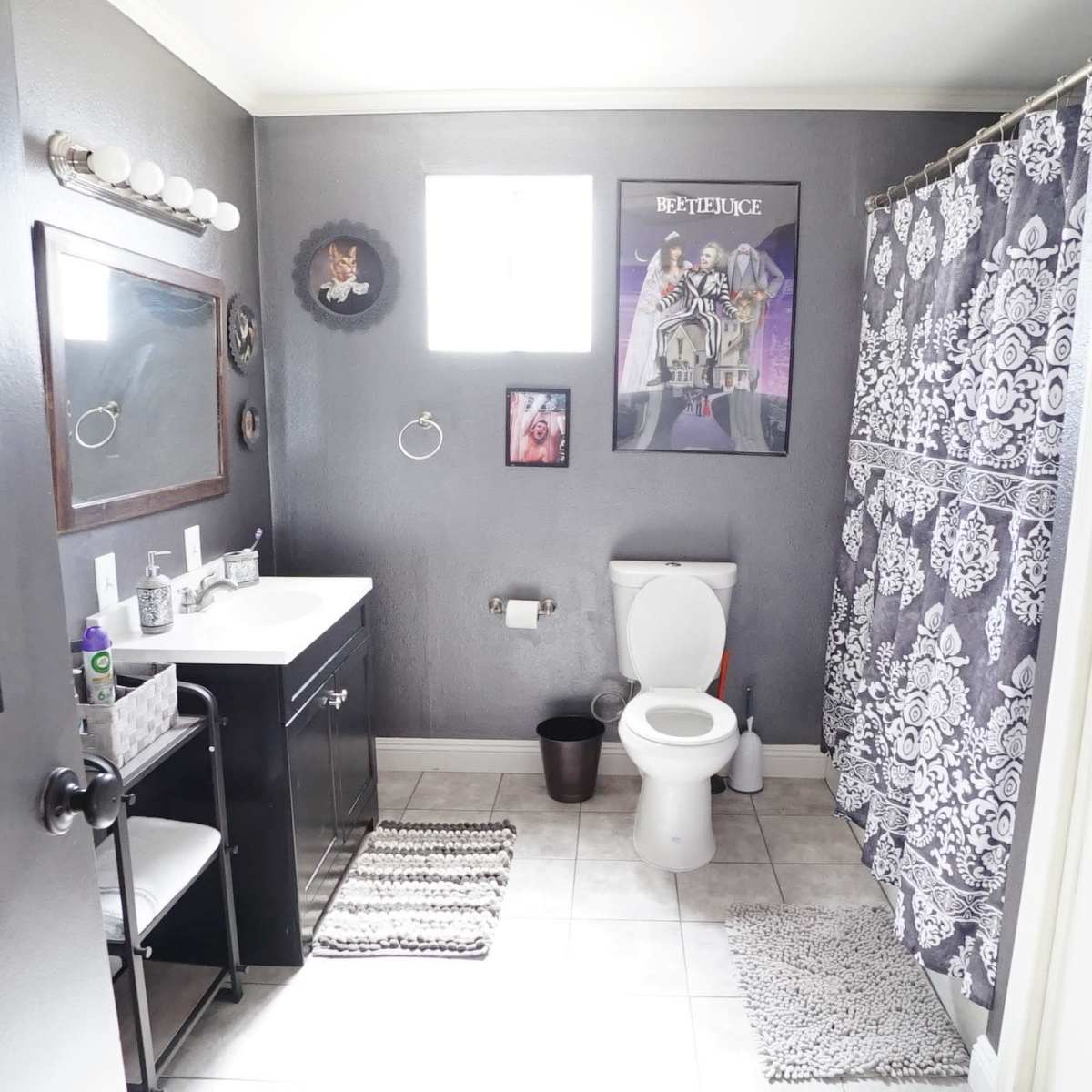 A bathroom with a gray color scheme, featuring a toilet, sink vanity, and a shower curtain, along with framed art on the walls.