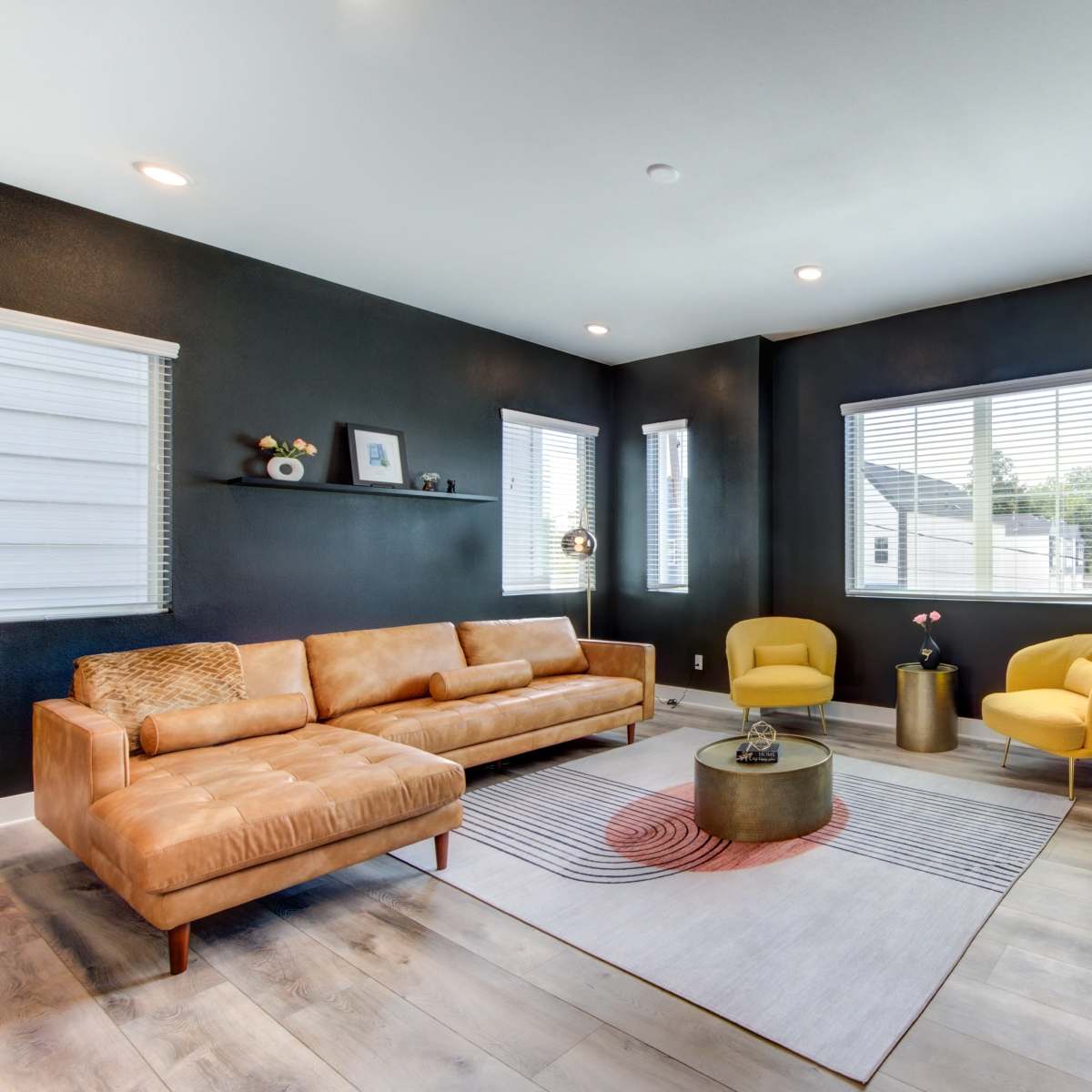 A modern living room with a brown leather sofa, two yellow chairs, a circular coffee table, and a large wall-mounted TV.