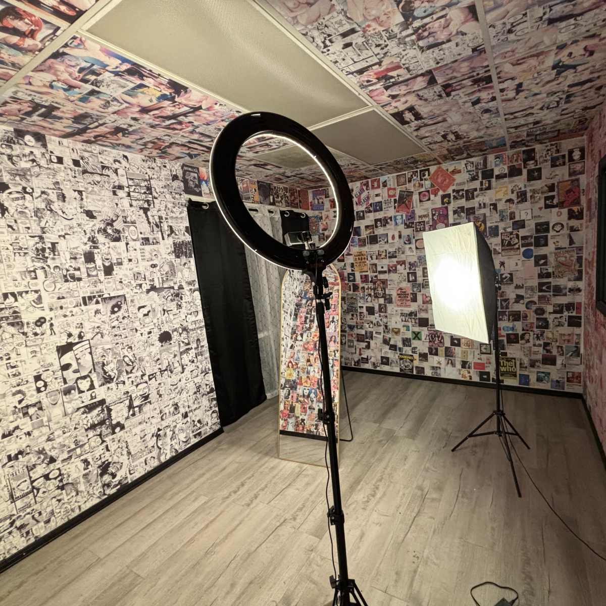 A small room with walls covered in black-and-white photographs and a ring light set up alongside a softbox lighting equipment.