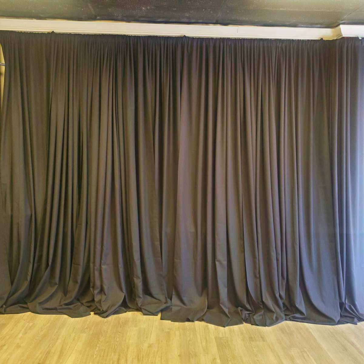 A black curtain draped on a wall, with a wooden floor visible below.