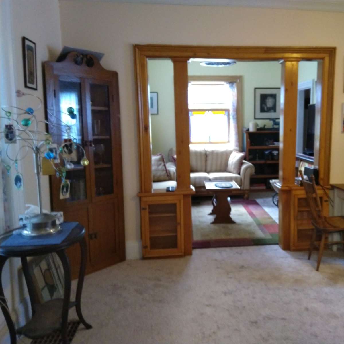 A living room area viewed from an adjoining room, featuring a wooden divider, a sofa, a television, and various decorative items.