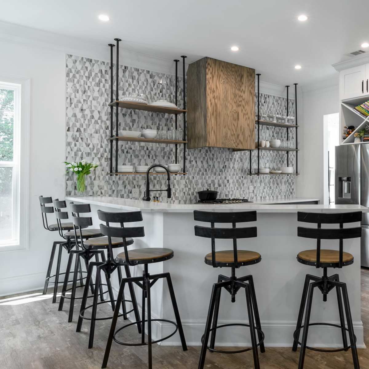A modern kitchen features a central island with bar stools, sleek cabinetry, and tiled backsplash.