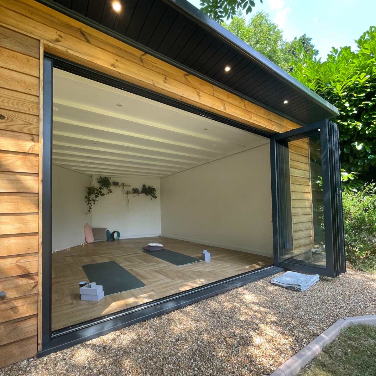 A spacious room with large glass doors that open to a gravel outdoor area, featuring wooden walls and minimalistic decor suitable for yoga or meditation.