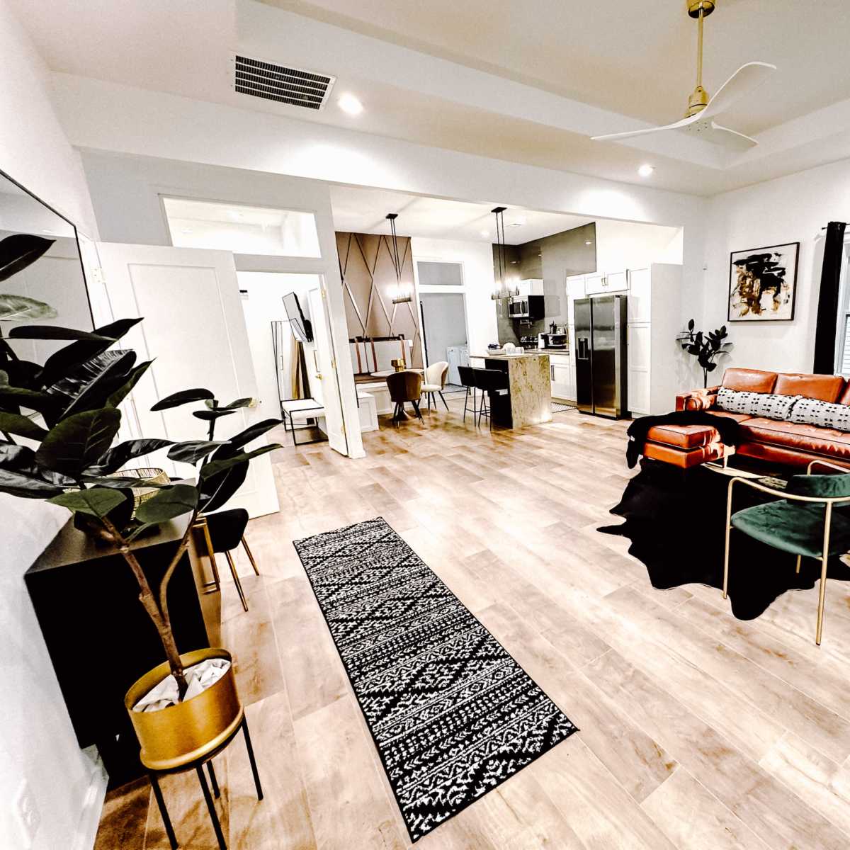 The spacious living area features a bright, open layout with a combination of modern furniture, including a coral sofa, plants, and a patterned area rug.