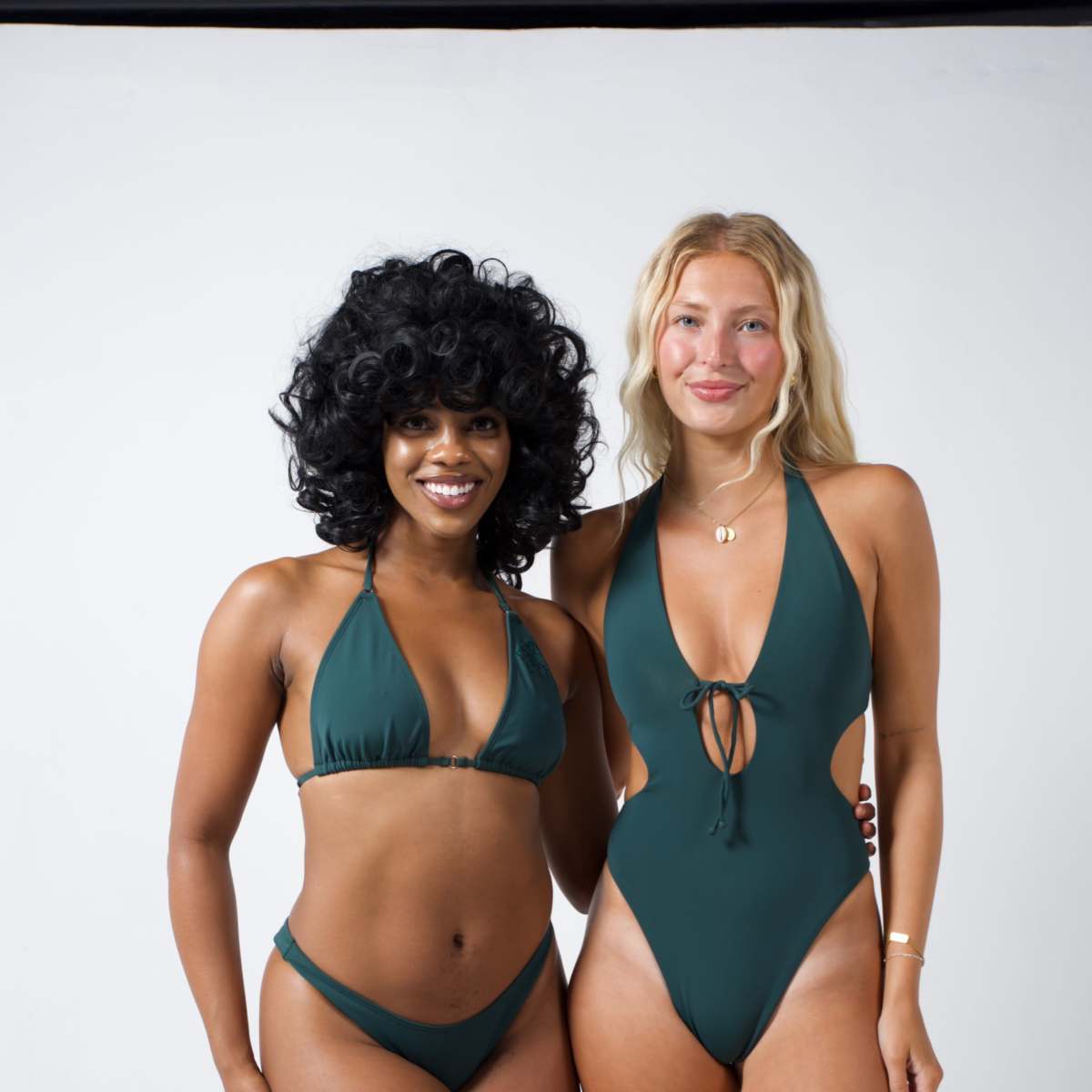 Two women are standing side by side, modeling green swimwear against a plain white background.