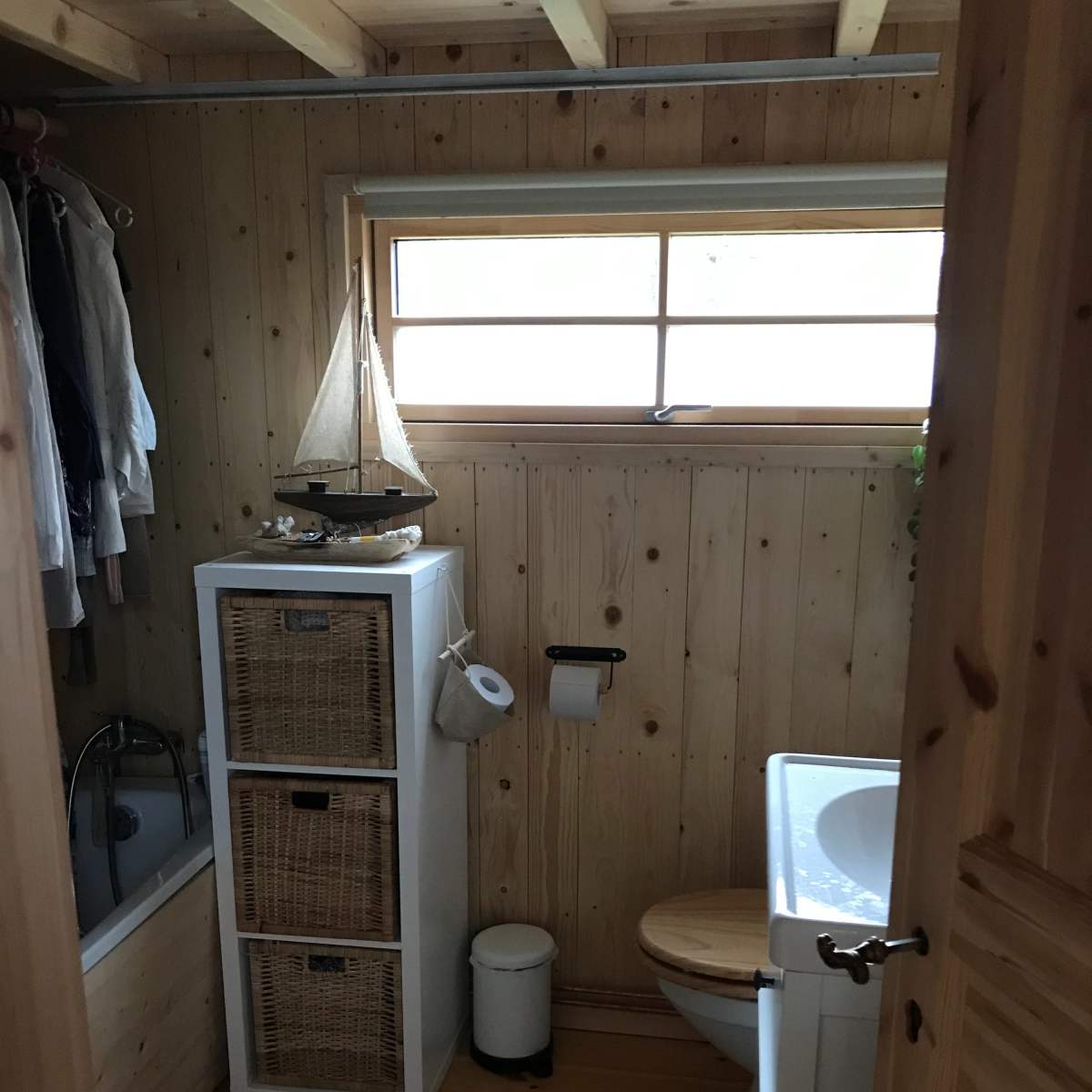 A small bathroom with wooden walls, a shower area, a sink, a cabinet for storage, and a sailboat decoration on top of the cabinet.