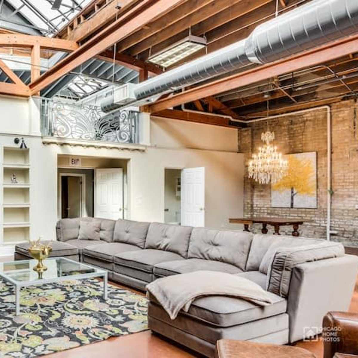 A spacious living area with a large sectional sofa, a coffee table, built-in shelves, and a chandelier, all beneath a skylight and wooden beams.
