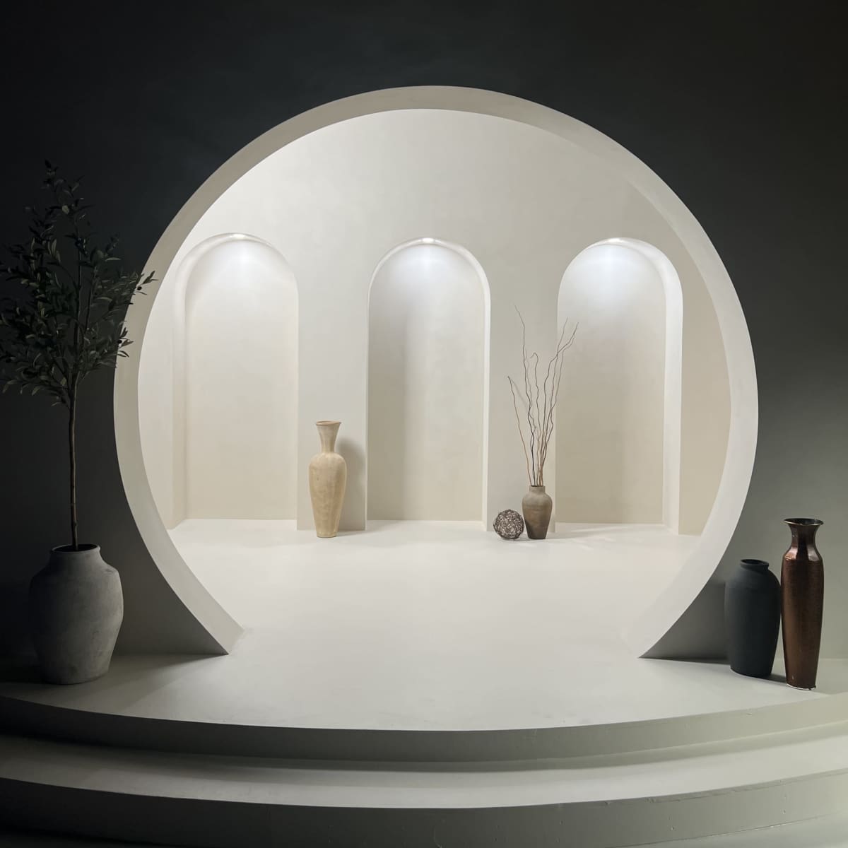A minimalist display niche with three arched alcoves, two vases, and decorative elements set against a softly illuminated background.