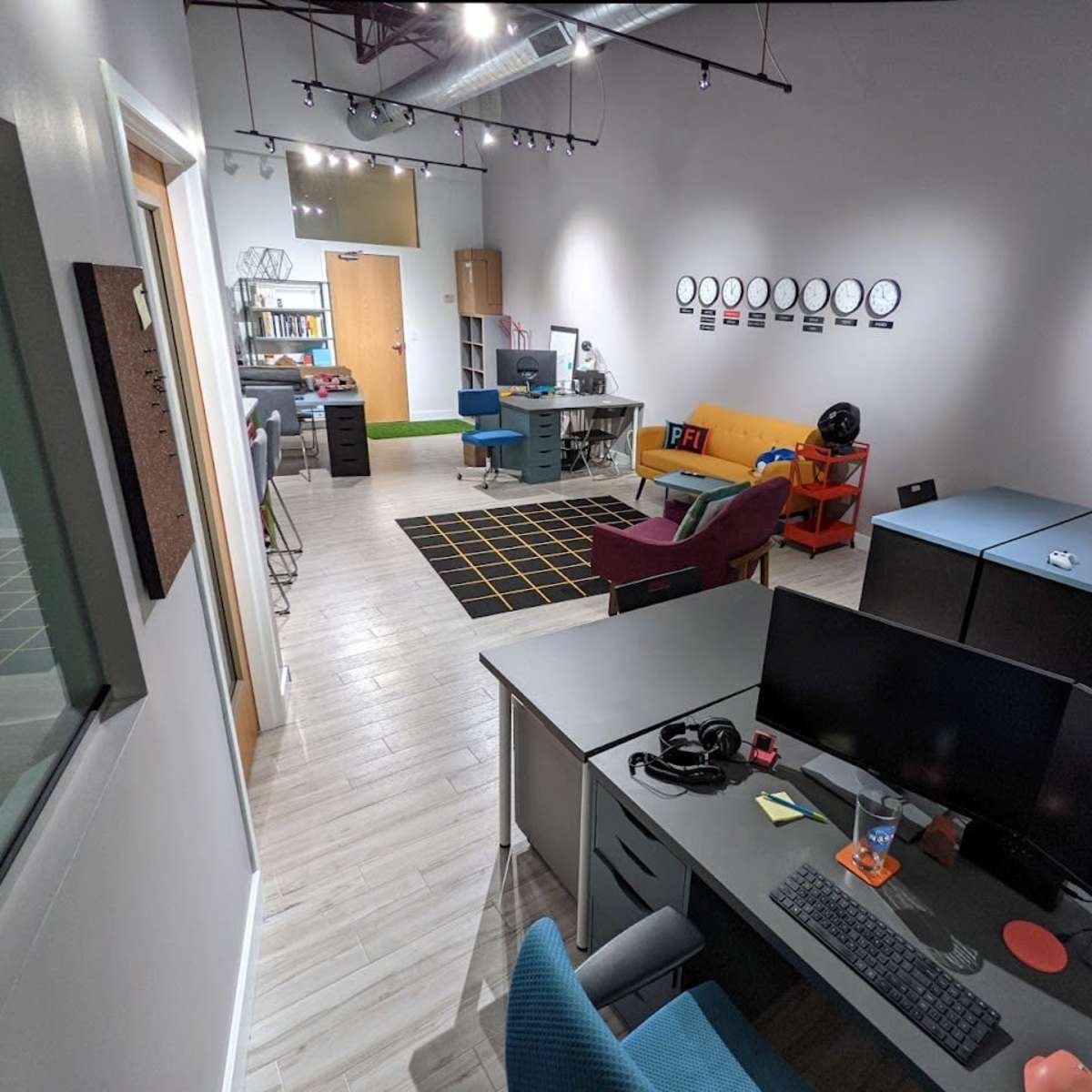 A modern office space with several workstations, a lounge area, and a wall featuring circular clock decorations.