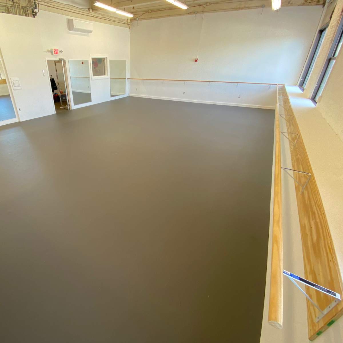 A spacious dance studio with a smooth gray floor, large mirrors on one wall, and a ballet barre running along another wall.