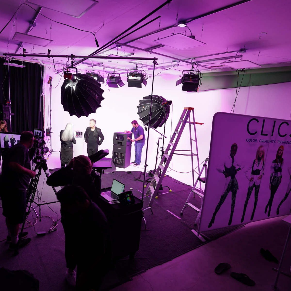 A photography studio setup features multiple lighting equipment, a large backdrop, and a team working on a photoshoot.