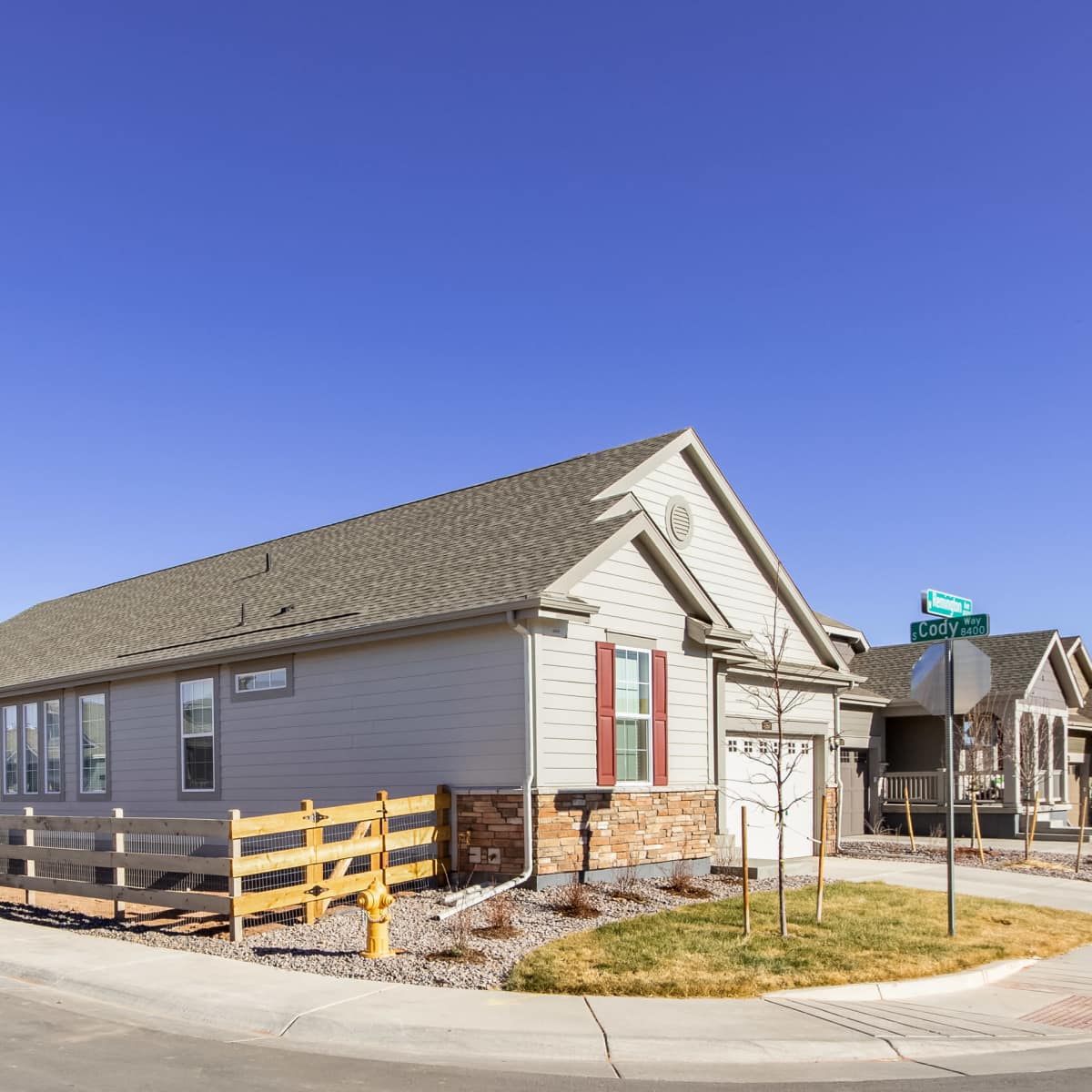 A single-story house with a gray exterior and a fenced yard is situated at the corner of a residential street.