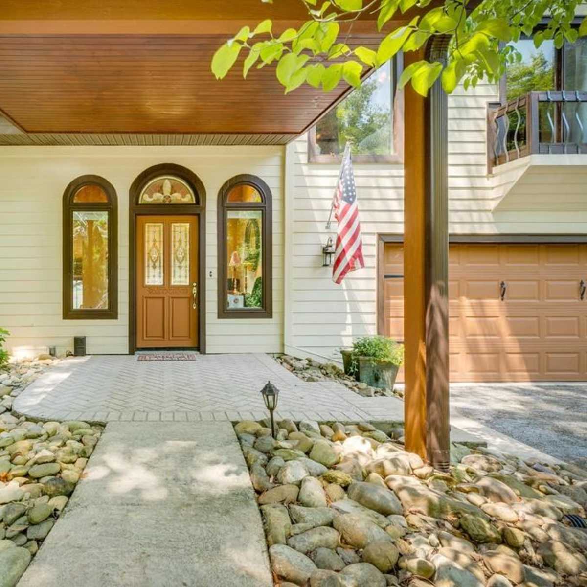 The entrance of a house with a stone pathway leading to a door under a covered porch and an American flag displayed.