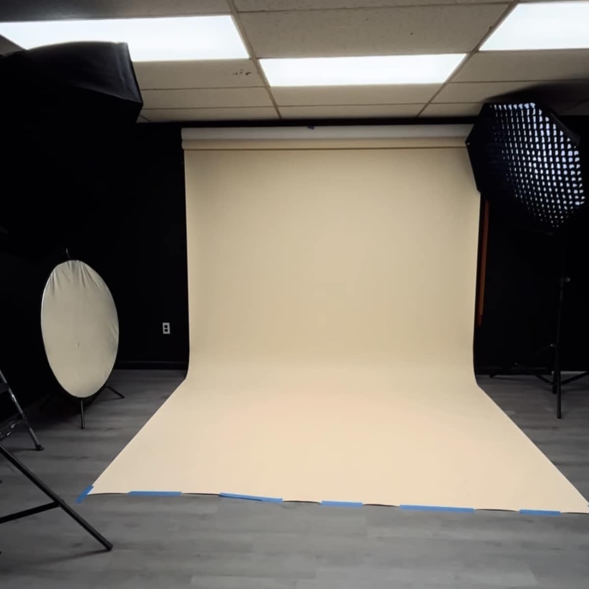 A photography studio with a seamless beige backdrop, two studio lights, and a circular reflector.