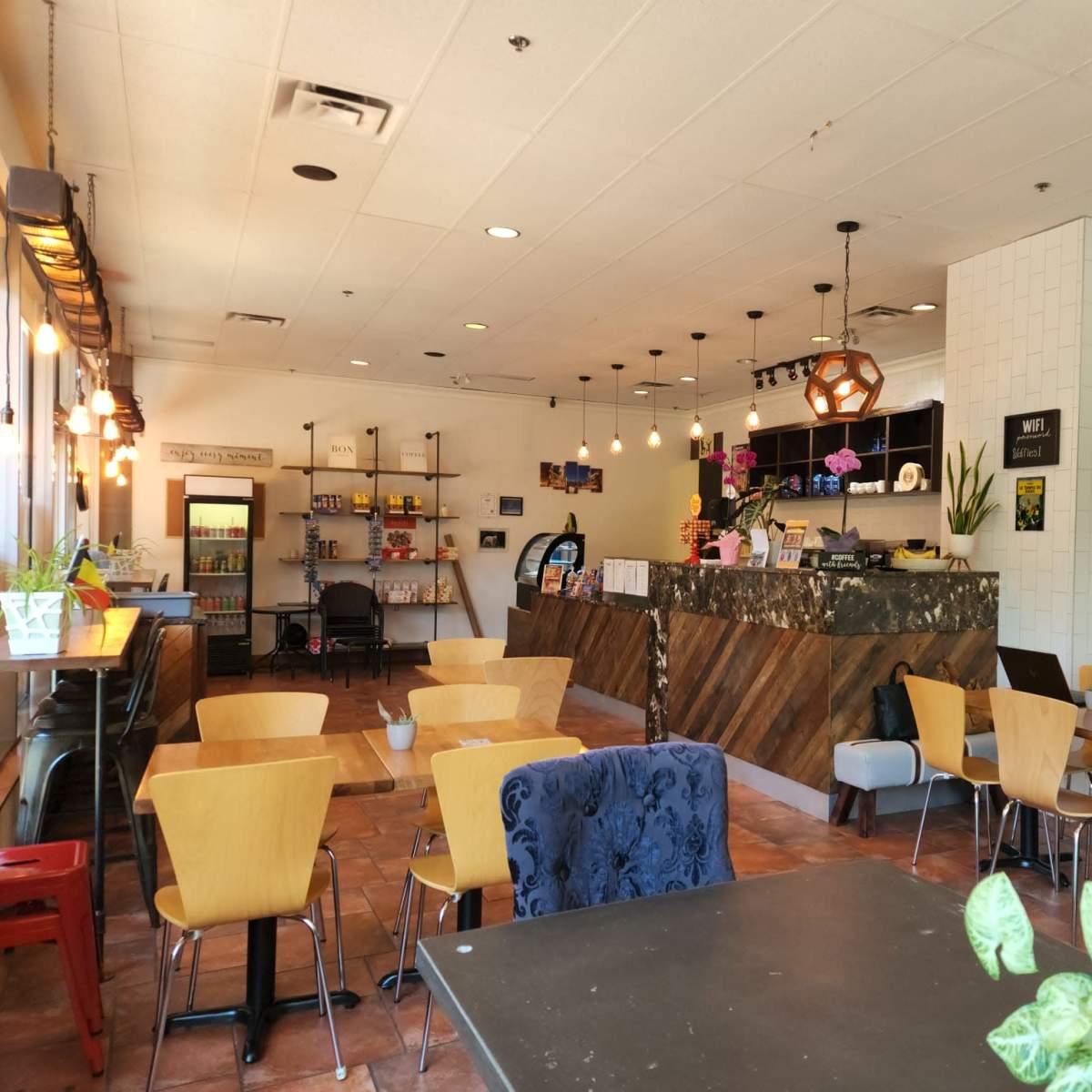 An interior of a café featuring a counter with a display, seating areas with wooden tables and chairs, and decorative lighting.