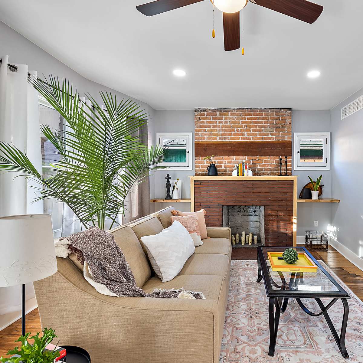 A cozy living room features a brick fireplace, a sofa, and a television mounted on the wall.