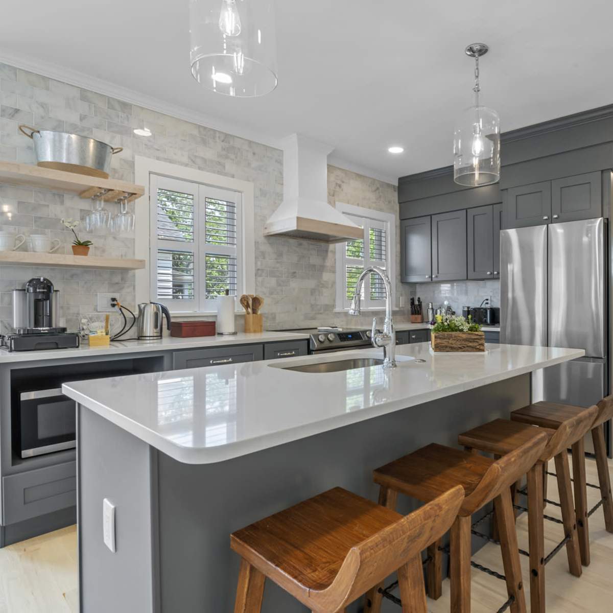 A modern kitchen featuring gray cabinets, a central island with bar stools, and stainless steel appliances.