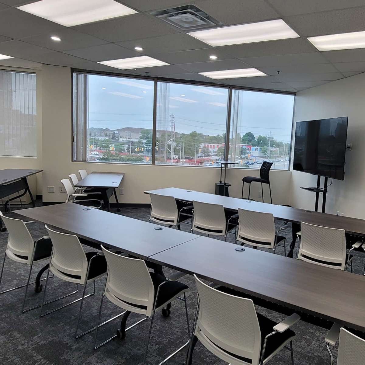 A modern conference room with several tables, chairs, and large windows overlooking an outdoor view.
