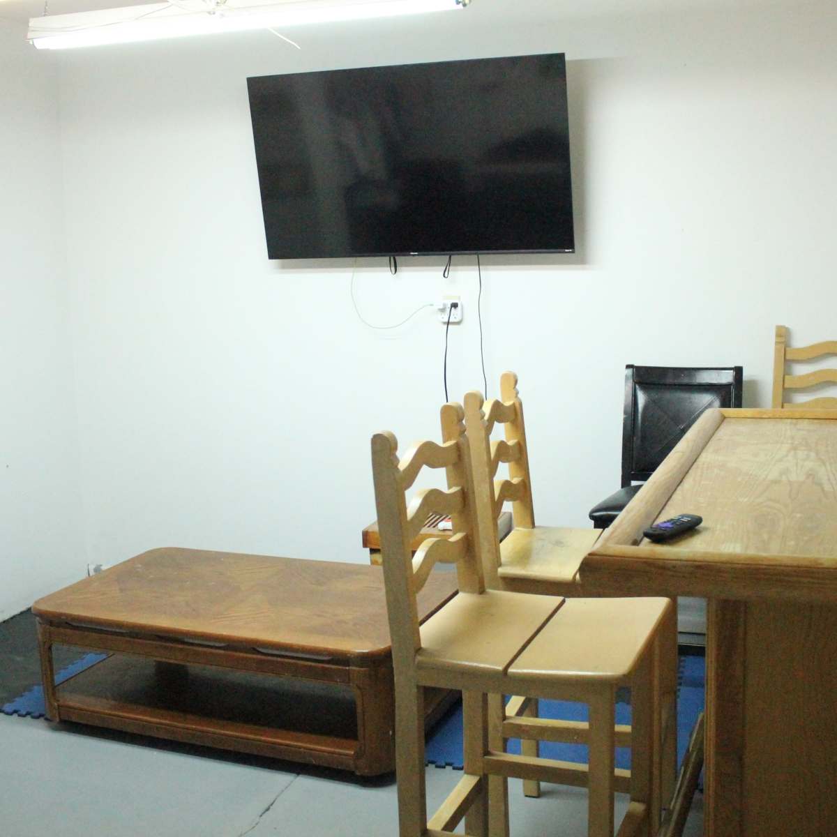 A small room with a wall-mounted TV, a wooden bar, a few chairs, and a low table on the floor.
