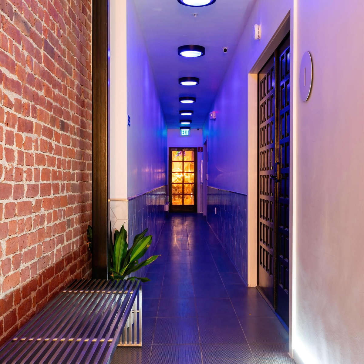 A long corridor with exposed brick walls, a metal bench, and illuminated circular ceiling lights.